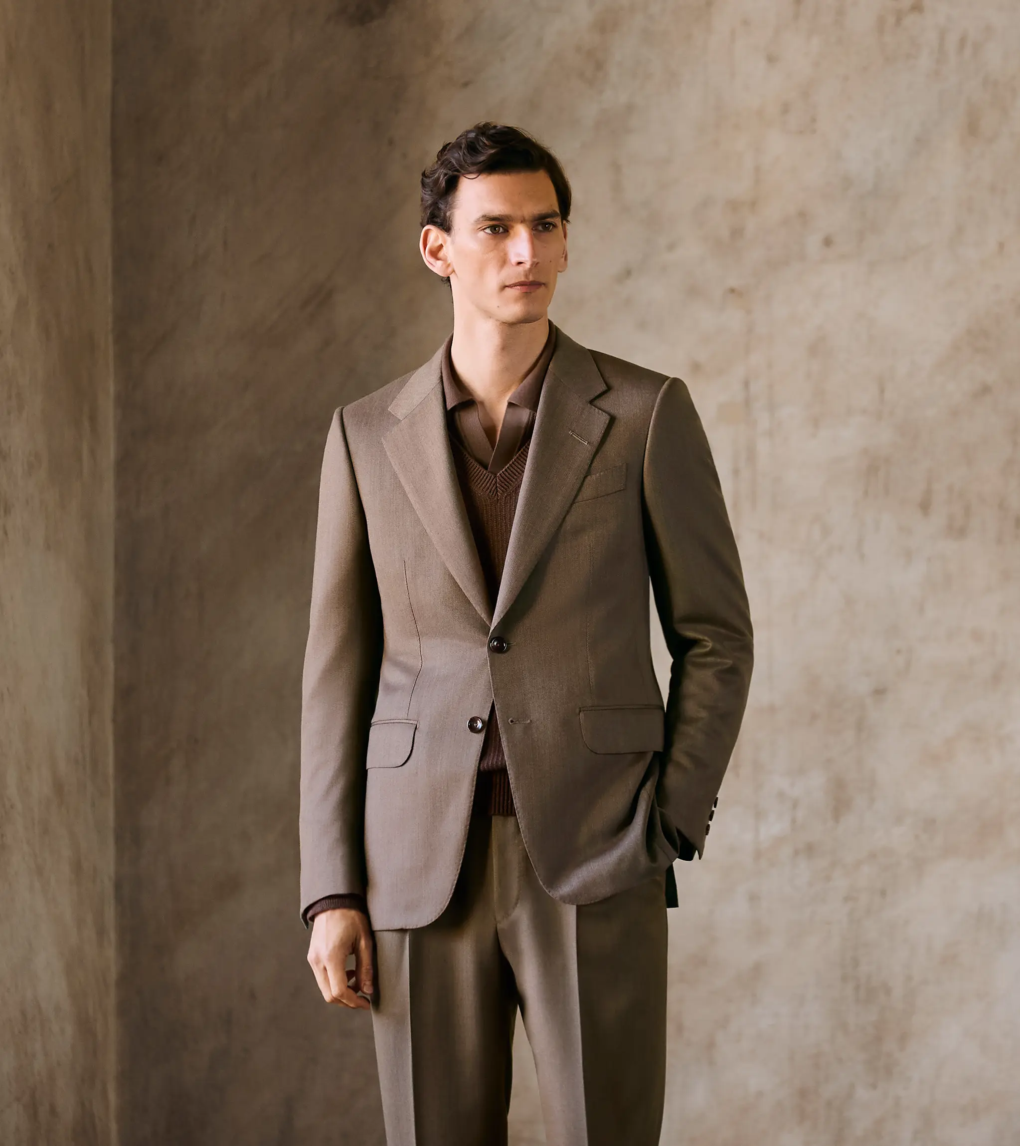 Ein Mann mit einem eleganten braunen Anzug mit einreihigem Jackett und einer Bügelfaltenhose von ZEGNA.
