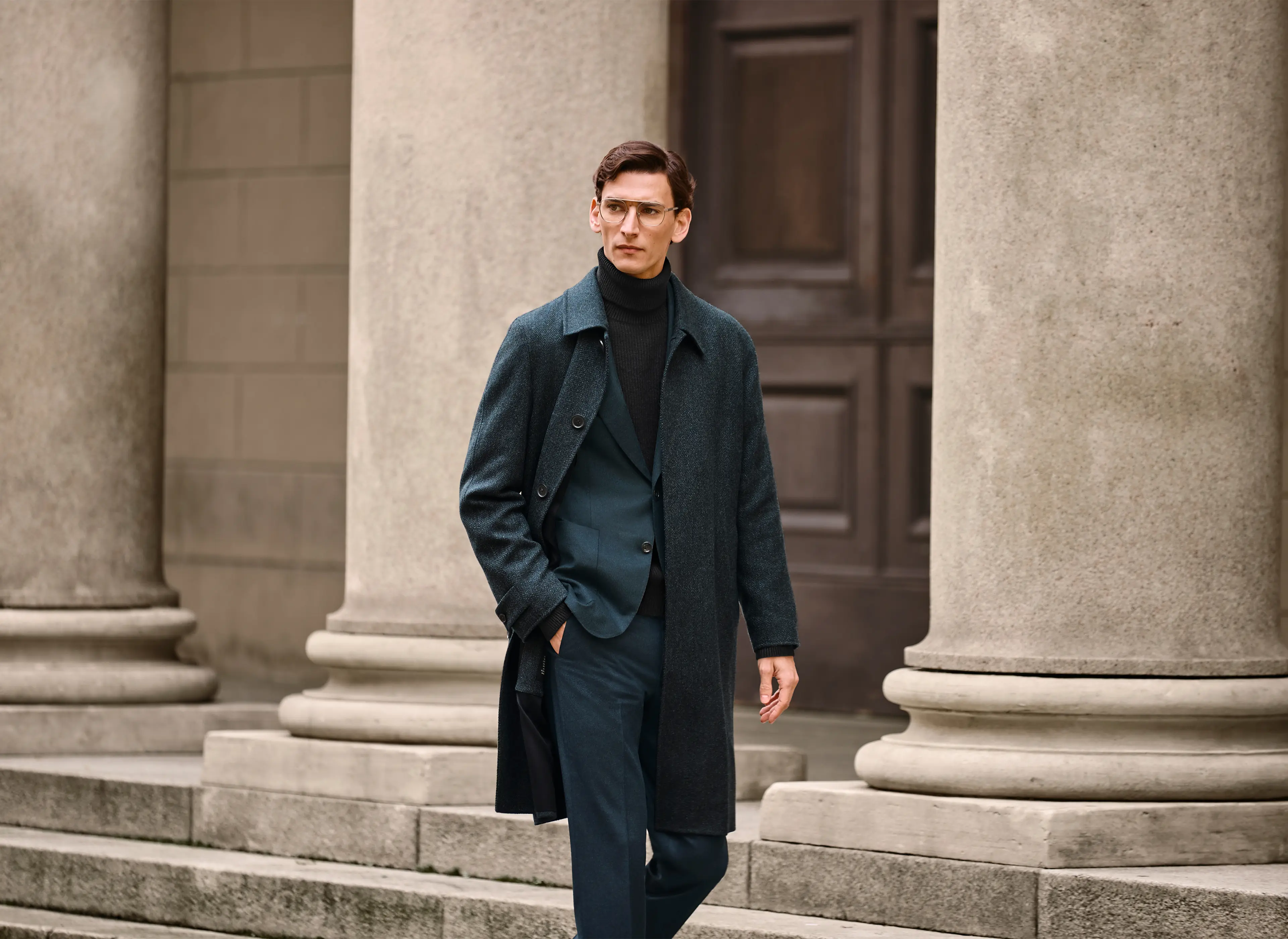 Ein Mann mit einem langen Mantel, eleganten Anzug und einem Rollkragenpullover aus Kaschmir aus der FW25-Kollektion von ZEGNA.